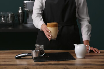 Female barista with glass of cold  coffee at table, closeup