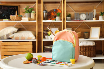 School backpack and paints on table in room