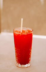 Refreshing red drink garnished with ice in a clear glass against a neutral background