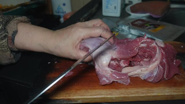 chopping raw beef meat on a chopping board. The meat is raw and has a lot of fat. Cooking preparation in the kitchen