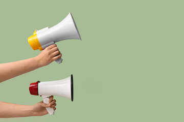 Female hands with megaphones on green background