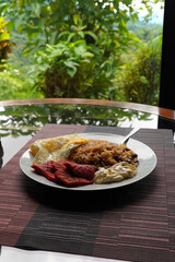 Gallo pinto, a typical Costa Rican dish with rice, red beans, sausage, cream, and a fried egg, and a glass of coffee on a table with a nature background.