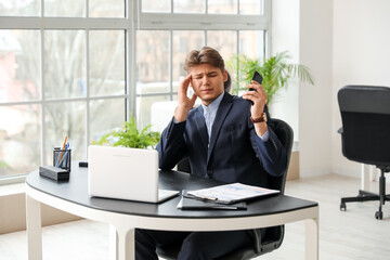 Young businessman with mobile phone suffering from headache in office