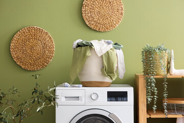 Laundry basket with dirty clothes on washing machine near green wall in room