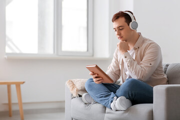 Young man listening music and reading book on armchair in living room