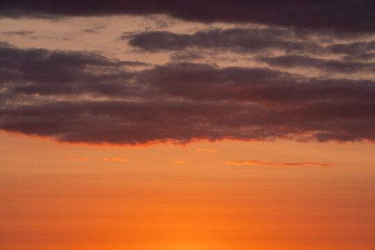 Texture of a beautiful sunset sky as an atmospheric photo background. Dark storm clouds contrast with the warm orange light of the setting sun.