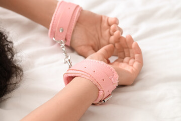 Young woman with pink handcuffs from sex shop lying on bed, closeup