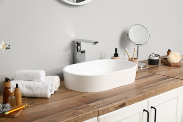 Modern sink and bath supplies on wooden chest of drawers near light wall in bathroom