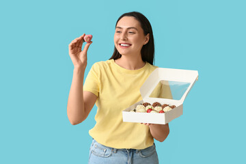 Beautiful young woman holding box with chocolate covered strawberries on blue background