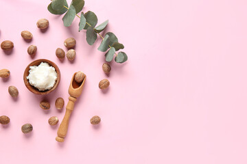 Bowl with shea butter, nuts and green twig on pink background