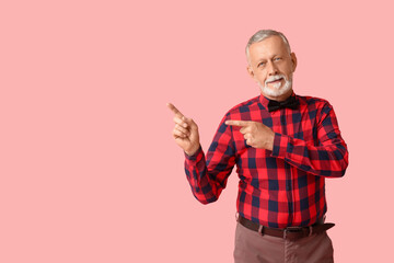 Fototapeta premium Handsome happy mature man with stylish bow tie pointing at something on pink background