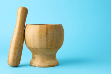 Wooden mortar and pestle on light blue background, closeup. Space for text