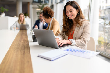 Smiling businesswoman working on project over laptop with colleagues during collaborative meeting...