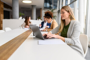 Confident female professional analyzing report over laptop while working with colleagues in the...