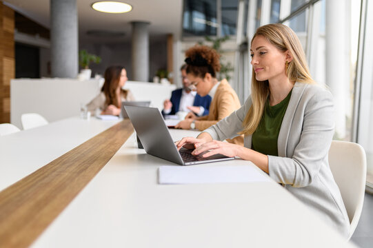 Confident female professional analyzing report over laptop while working with colleagues in the meeting room