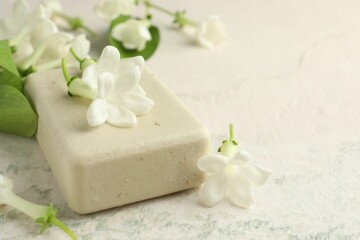 Bar of soap and jasmine flowers on light table, closeup. Space for text