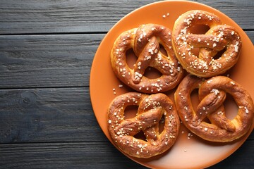 Tasty pretzels with salt on dark wooden table, top view. Space for text