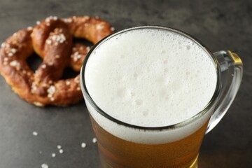 Glass of beer and tasty pretzel on dark textured table, selective focus