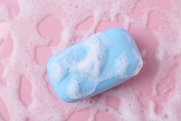 Soap bar with foam on pink background, top view