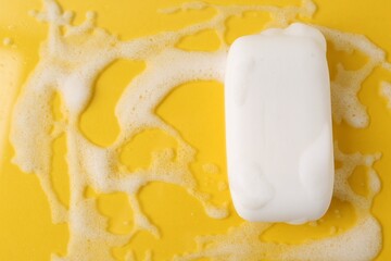 Soap bar with foam on yellow background, top view. Space for text