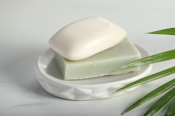 Soap bars and palm leaf on white marble table, closeup
