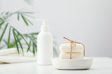 Soap bars and bottle on white table against grey background, selective focus