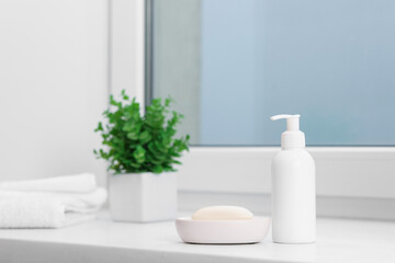 Fototapeta premium Soap bar, bottle of cosmetic product, towels and floral decor on white window sill indoors