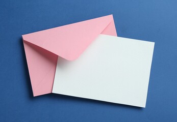 Blank invitation card and envelope on blue background, top view. Space for design