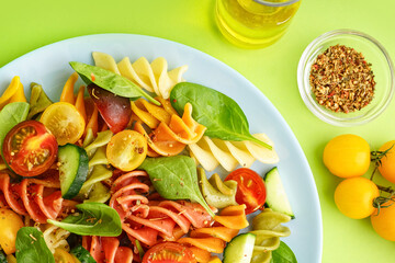 Plate with Italian pasta salad on green background