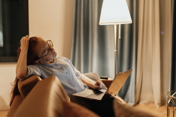 Woman leans back on sofa with hand on head and laptop on lap showing mental overload digital fatigue and slow living in tech era reflecting emotional exhaustion from constant online engagement