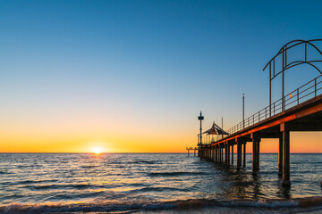 Brighton Jetty with sea views from beach as sun drops behind horizon on summer evening