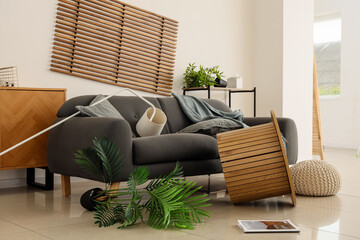 Interior of messy room with stylish sofa and overturned furniture after earthquake