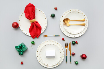 Beautiful table setting with Christmas balls and gift box on grey background