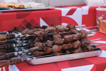 Ready pork shashlik on skewers cooling on an iron tray. Appetizing street food, freshly cooked juicy meat at a city festival. Close-up