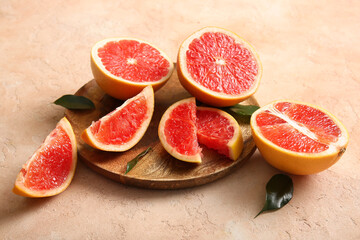 Wooden plate with cut fresh grapefruits and leaves on beige background