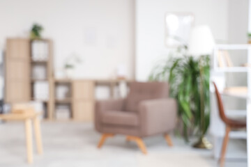 Blurred view of light office with armchair, plants and shelf unit