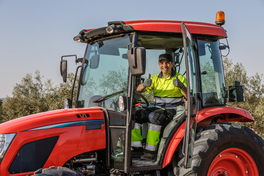 Farmer operating a red tractor in an olive grove under sunny skies