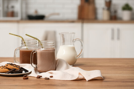 Mason jars of sweet chocolate milk and plate with tasty cookies on wooden table in kitchen