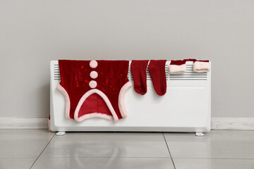 Santa Claus costume on heating radiator near grey wall