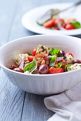 Simple salad with cherry tomatoes, feta cheese, kalamata olives, red pepper and fresh herbs. Bright wooden background. Close up.	