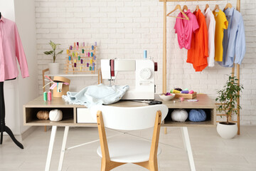 Tailor's workplace with sewing machine, different supplies and clothes rack in atelier