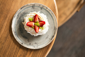 Pavlova cake with whipped mascarpone cream and fresh strawberry slices in cafe.