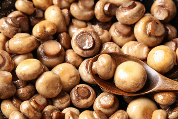 Wooden spoon with roasted mushrooms in frying pan, closeup