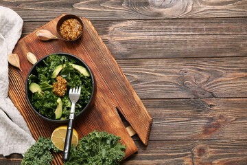 Board with bowl of tasty kale salad, avocado, Dijon mustard and avocado on wooden background