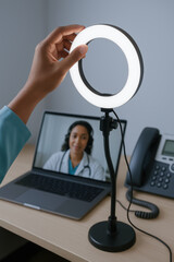 Healthcare patient adjusts ring light during tech consultation call with medical professional at center providing remote healthcare services