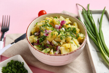 Bowl of tasty potato salad with onion and dill on pink background