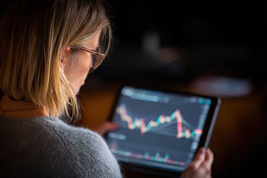 Focused businesswoman analyzes fluctuating stock market data on a digital tablet, illustrating modern financial trading insights and investment decision-making process