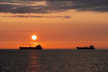 Fototapeta premium Silhouettes of two oil tankers against an orange sunset in the Baltic Sea. Maritime oil transportation, Estonia.