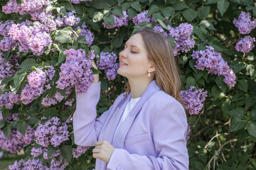 A beautiful young blonde woman, against a background of blooming lilacs, in a lilac trouser suit....