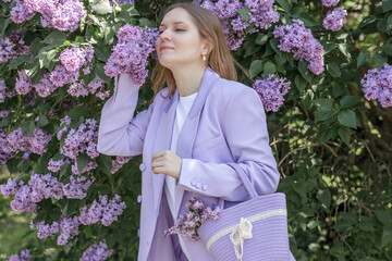 A beautiful young blonde woman, against a background of blooming lilacs, in a lilac trouser suit....